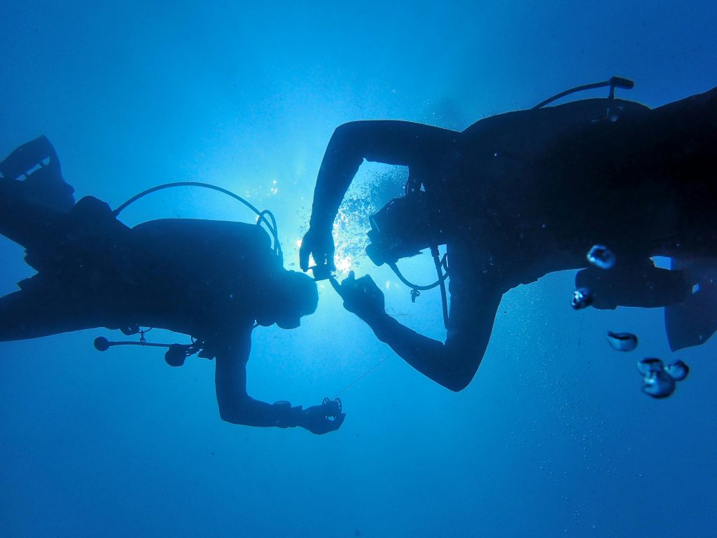 Silhouette of two scuba divers sharing a moment underwater in a bright blue ocean scene.